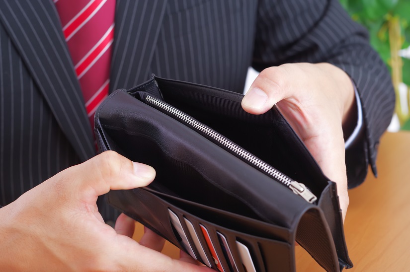 空っぽの財布を広げるワイシャツ姿の男性